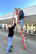 Brian Sanders, on ladder, and Larry Stendebach, on the ground, begin to set-up KSFF banner